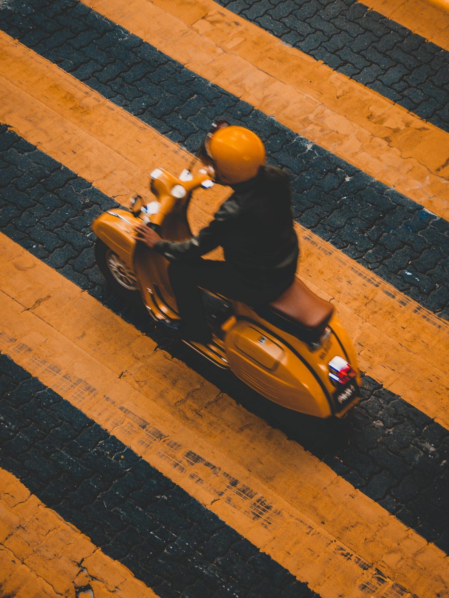A yellow scooter driving over a yellow crosswalk.