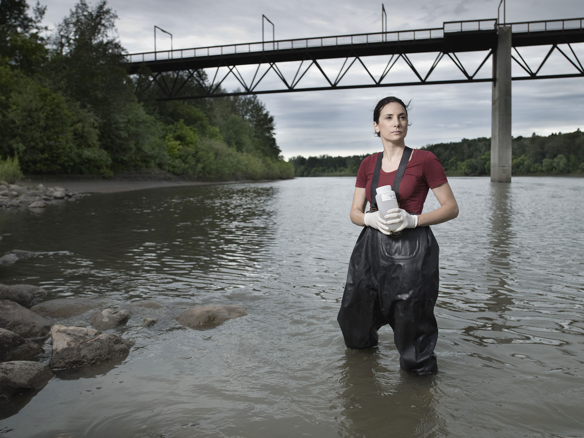 steph neufeld stands knee-deep in gaiters and holds container in river